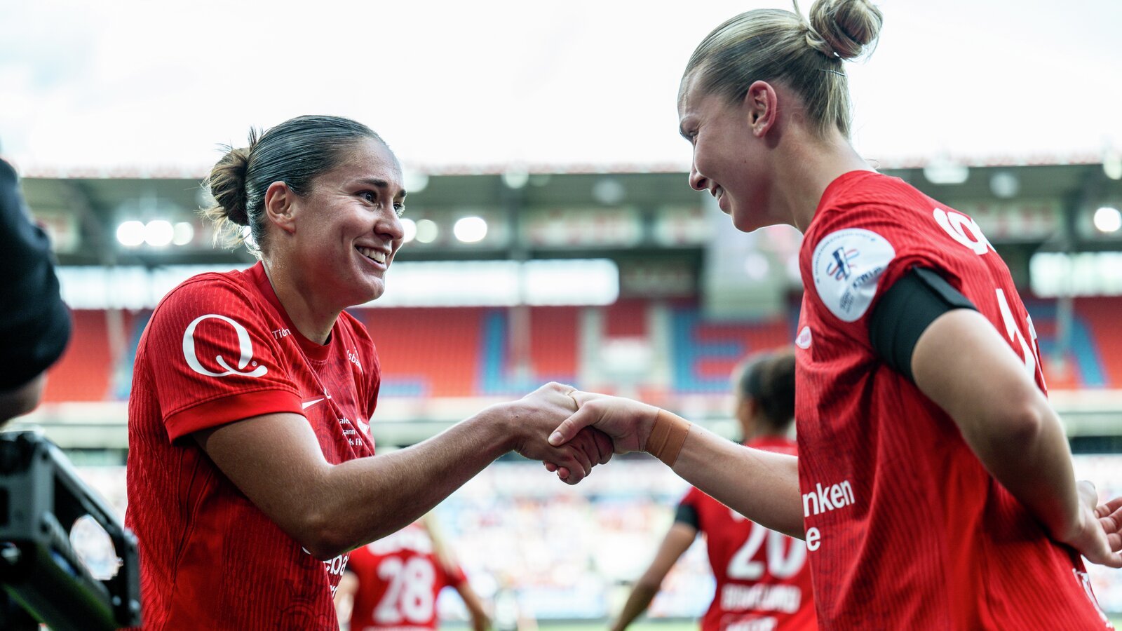 To fotballspillere i røde uniformer feirer sammen, og lager et hjerte med hendene på banen.