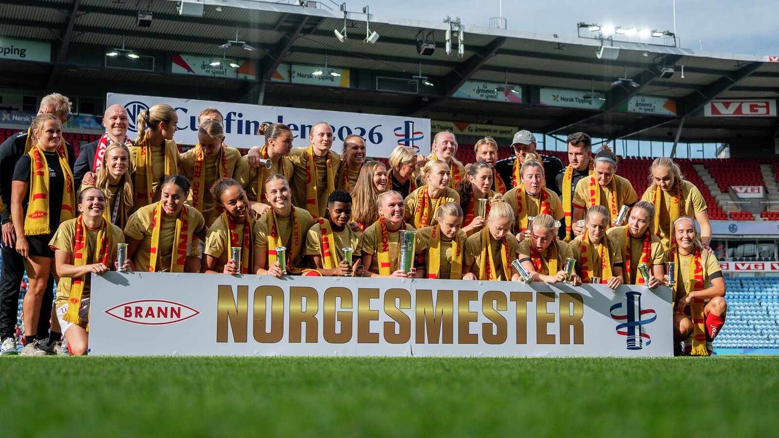 SK Branns kvinnelag i fotball feirer som norgescupmestere, poserer med Norgesmester-banner på stadion.